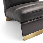 Close-up of a modern lounge chair or sofa corner in dark charcoal gray leather with brushed gold metal legs and base trim, photographed on a clean white studio background.