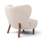 Three-quarter back view of the Little Petra Lounge Chair upholstered in off-white sherpa with walnut legs | Nue Modern