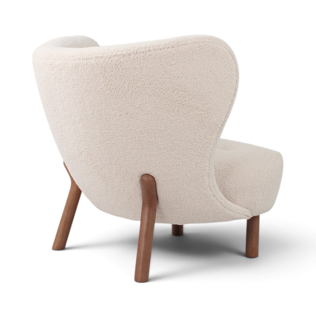 Three-quarter back view of the Little Petra Lounge Chair upholstered in off-white sherpa with walnut legs | Nue Modern
