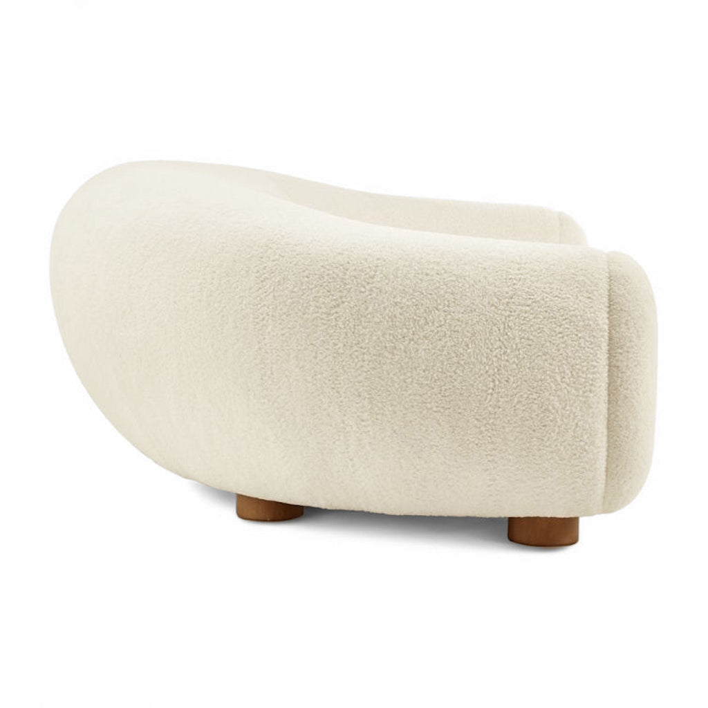 Side view of the curved Polar Bear Sofa in off-white sherpa showing its rounded back and short wooden legs | Nue Modern