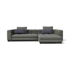 A modern gray fabric sectional sofa with a right-facing chaise lounge, featuring two dark purple accent pillows, shown against a plain white background.