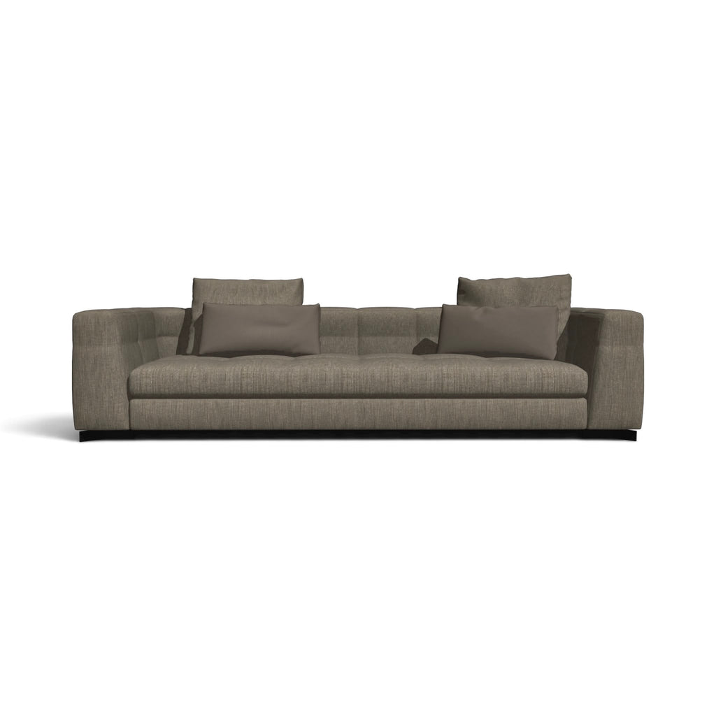 A modern three-seater sofa upholstered in textured taupe-gray fabric, featuring four matching throw pillows and a low black base, shown against a plain white background.